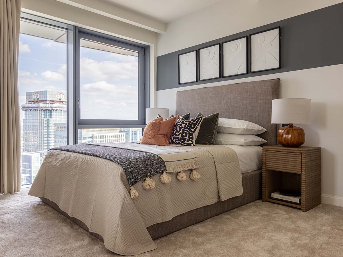 A modern bedroom at Aspen, Marsh Wall, with a city view, a grey upholstered bed, and a colour-block accent wall with white 3D art panels