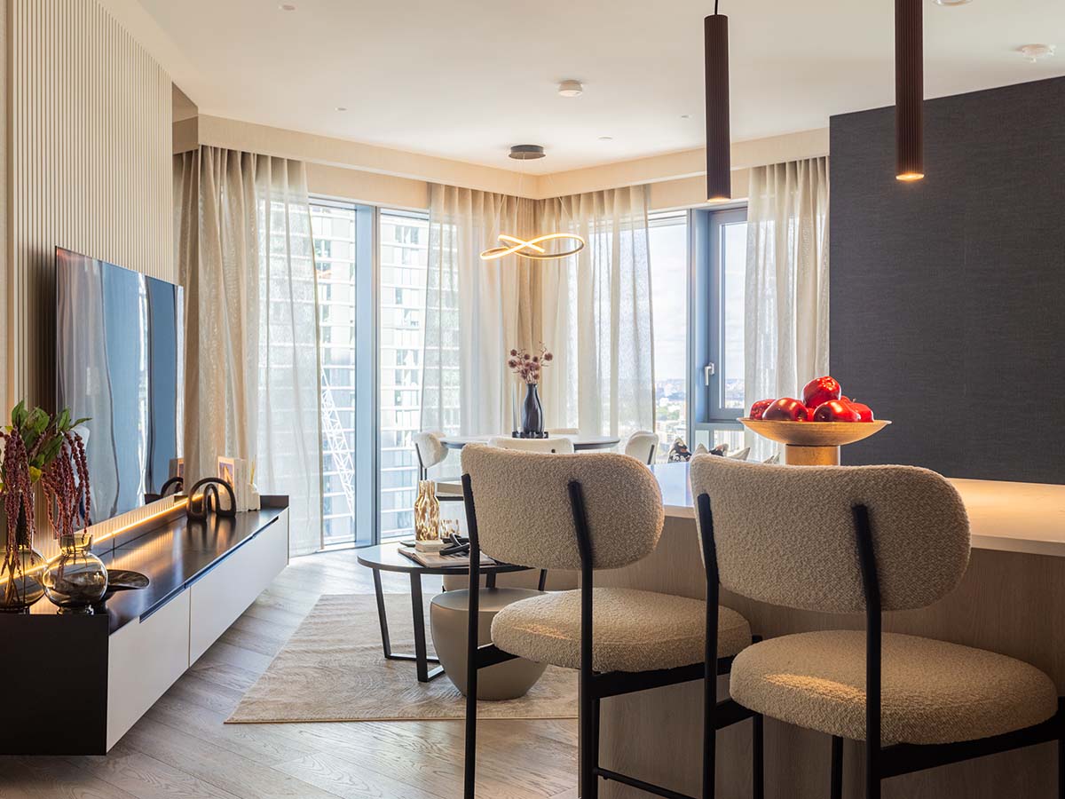 A wide view of a luxury open-plan apartment at the Aspen project, showing boucle bar stools, a modern dining area, and a slatted media wall