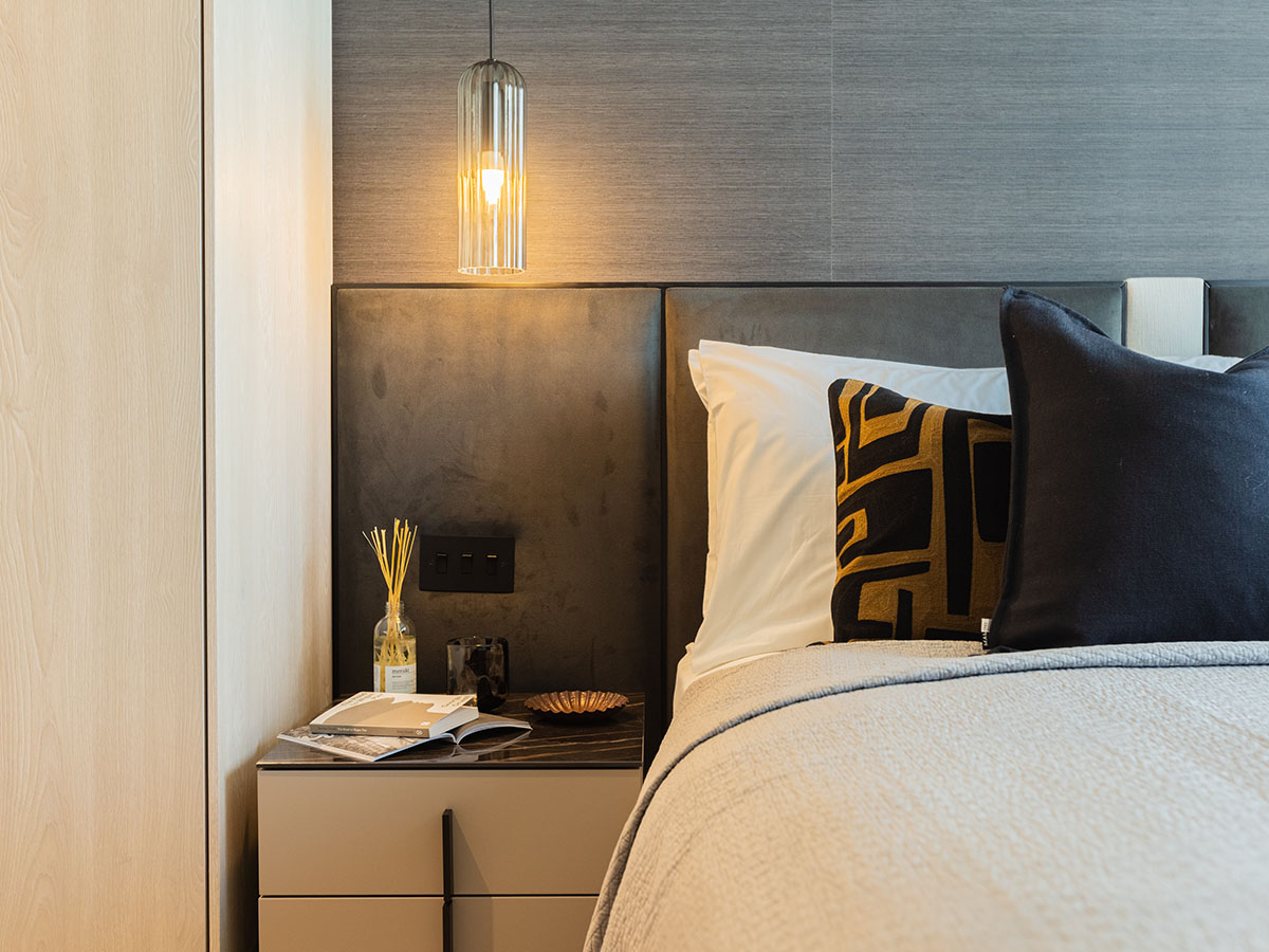 A close-up of a modern bedroom at the Aspen project, showing a styled bedside table with a contemporary glass pendant light hanging above