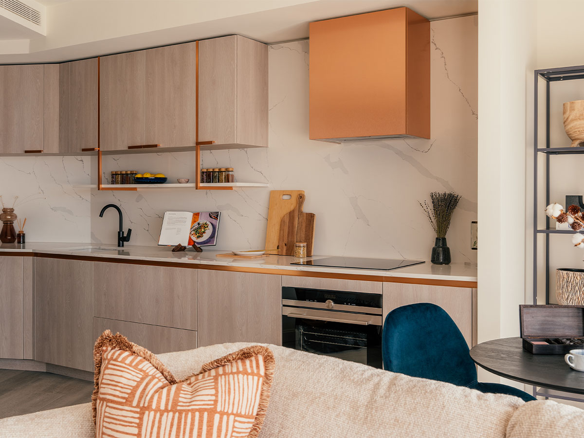 A stylish modern kitchen at the Aspen project, featuring light wood cabinets, a marble backsplash, and a statement copper extractor hood and trim