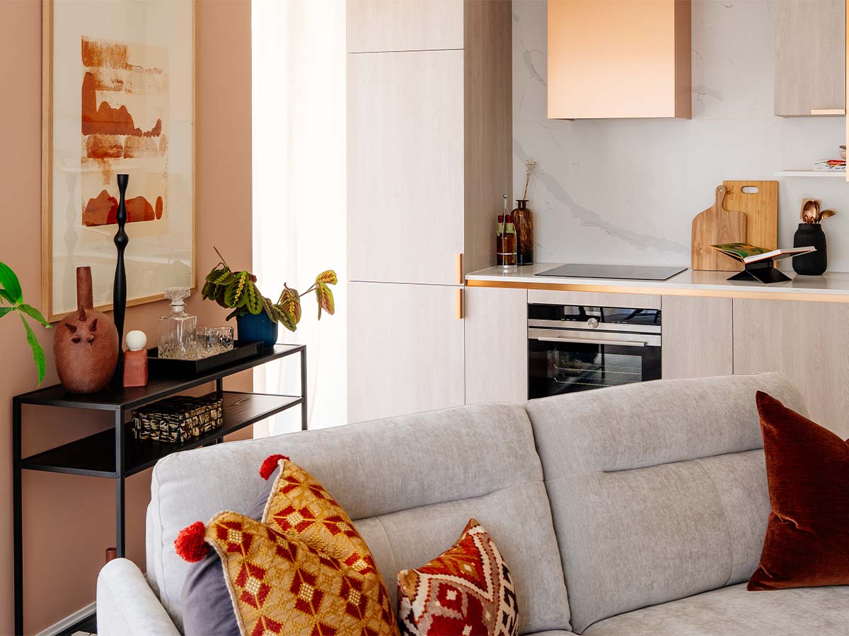 A modern open-plan living area at the Aspen project, showing a grey sofa and a view to the kitchen which features a statement copper extractor hood