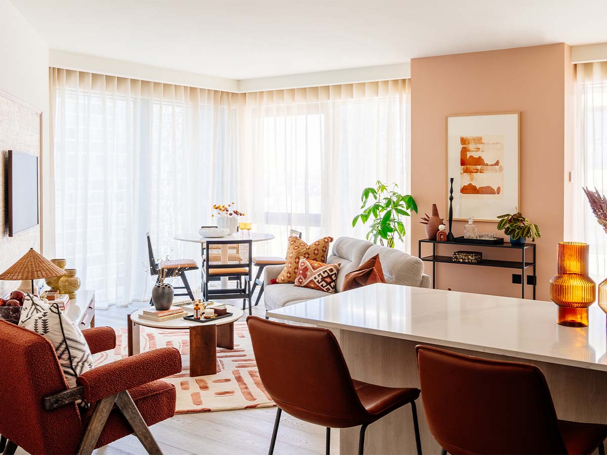 A bright, open-plan apartment at the Aspen project with warm terracotta walls, a rust-coloured armchair, and leather bar stools at the kitchen island