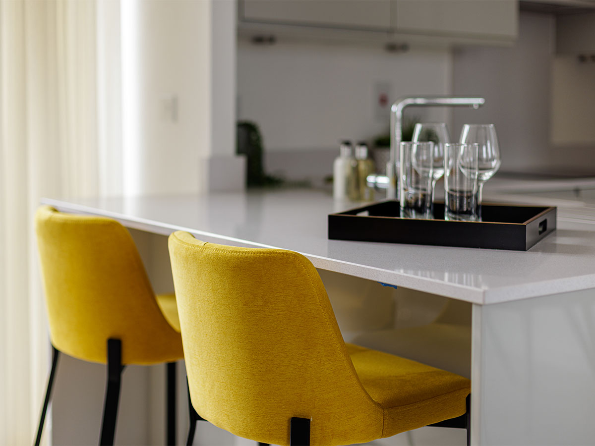 A sleek white kitchen island featuring two vibrant yellow upholstered bar stools that add a pop of colour to the modern space