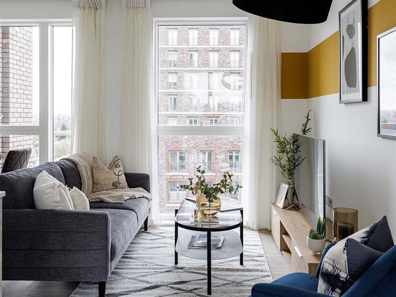 A modern living room at Cargo House featuring a dark grey sofa, a geometric rug, and a distinctive mustard yellow paint stripe on the wall above the TV