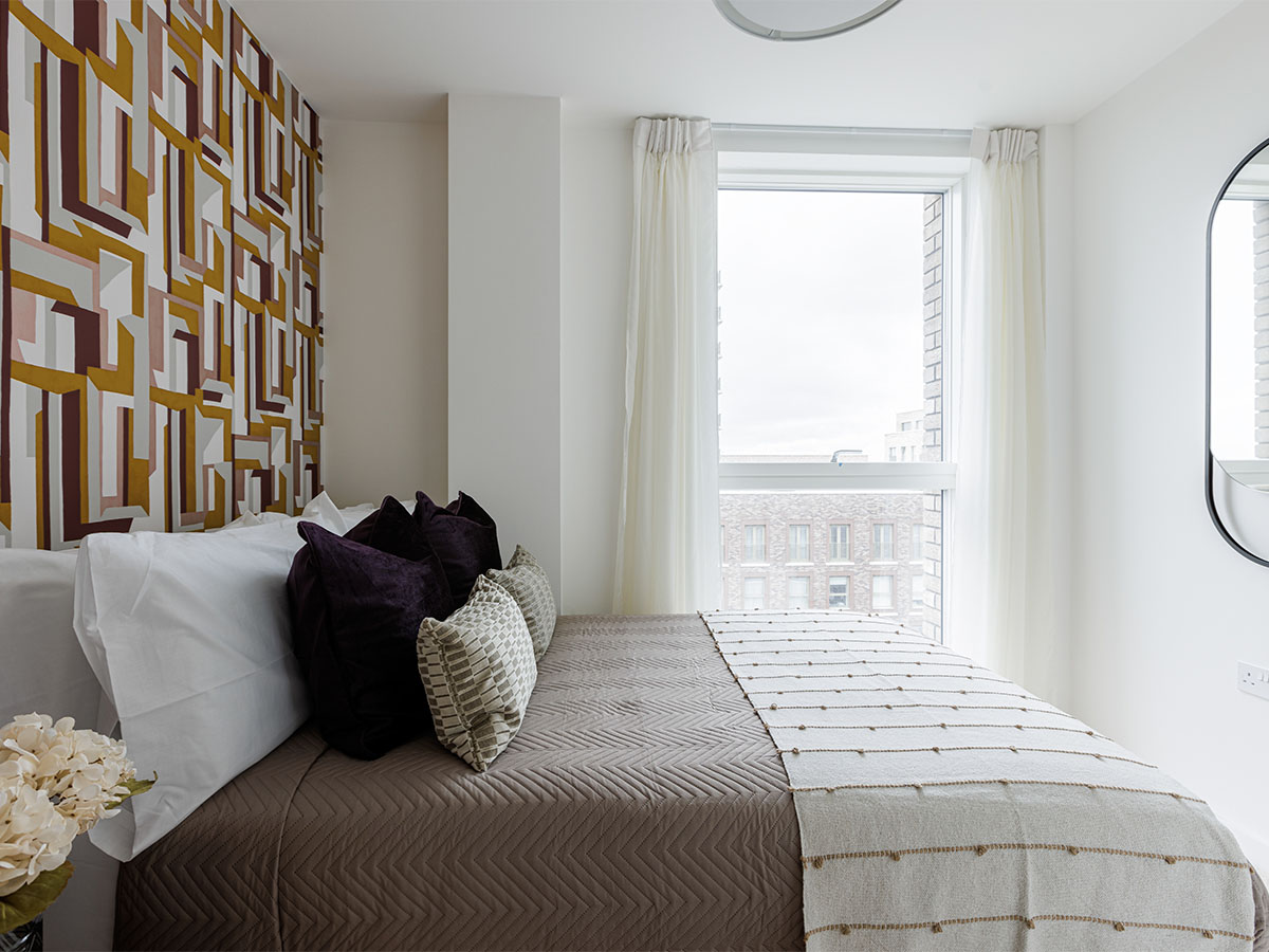 A modern bedroom featuring a bold geometric wallpaper in gold and brown tones, with a bed styled with deep purple velvet cushions