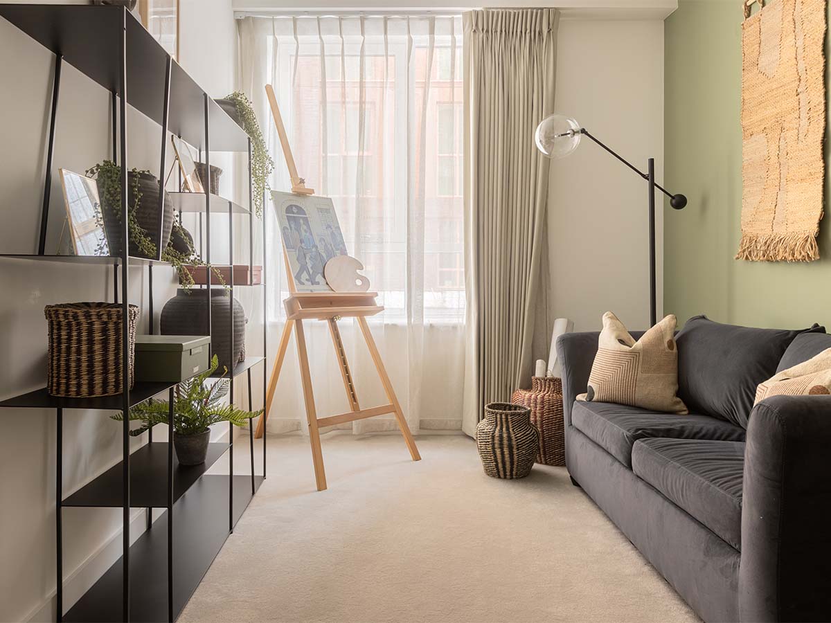 Living area with grey sofa, black shelves, and artist's easel