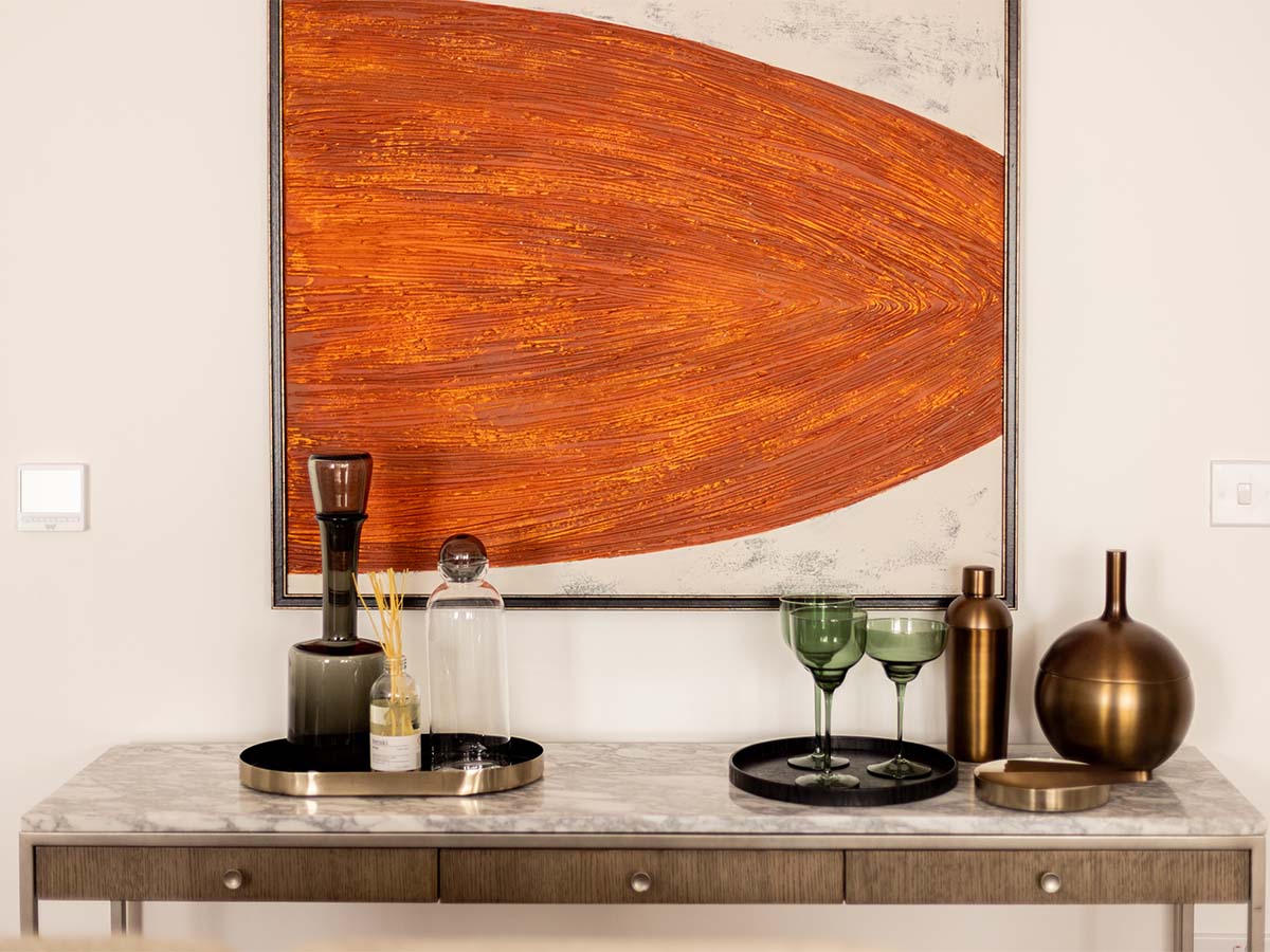 Decorated console table featuring trays, glassware, and orange art