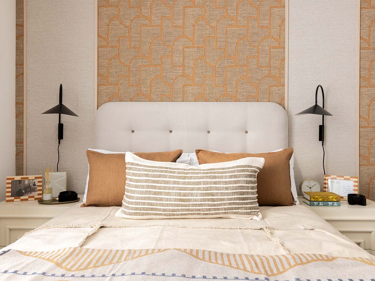 Bed with beige headboard, striped pillow, against geometric wallpaper