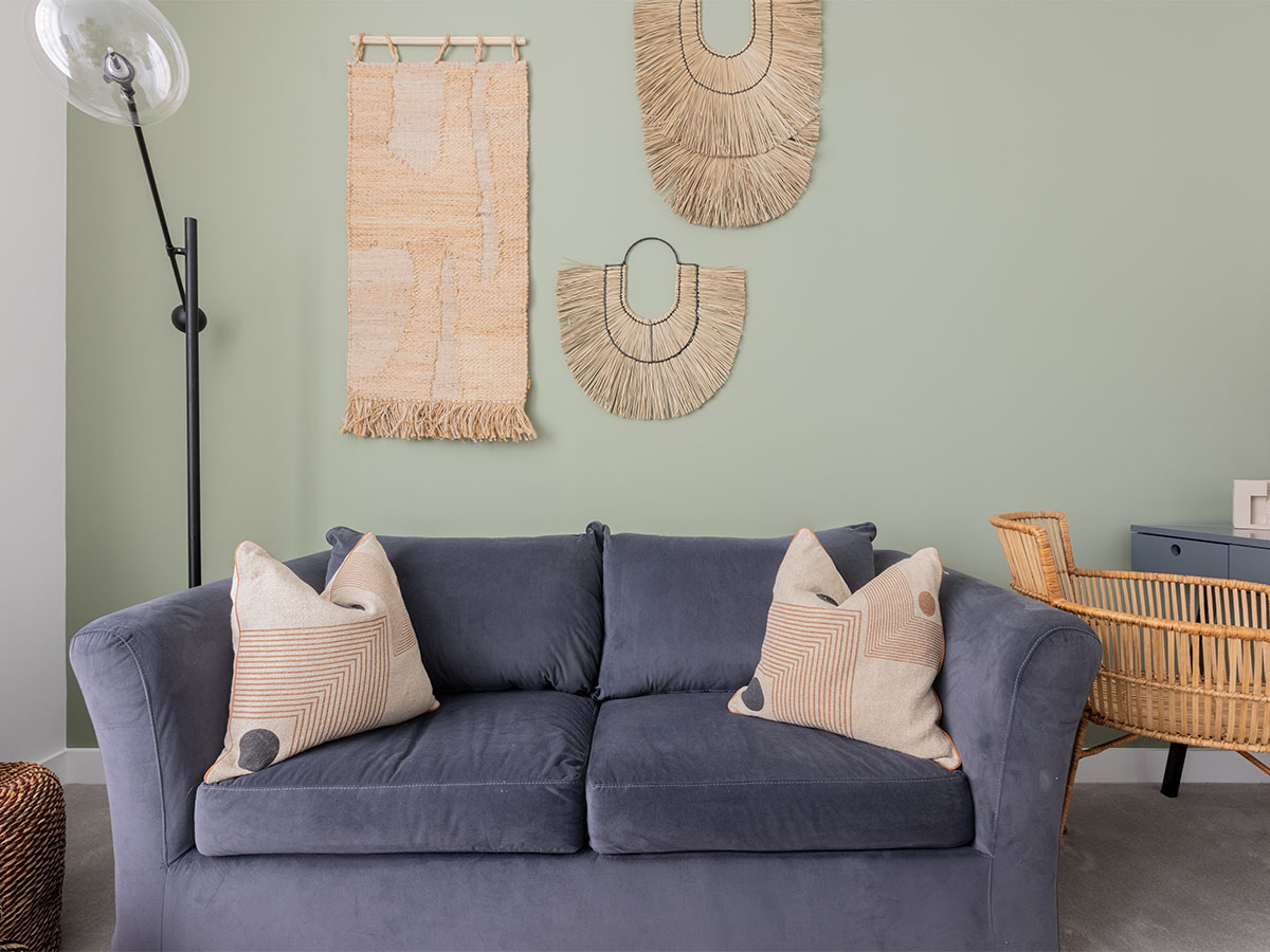 Charcoal sofa with cushions, raffia wall decor, and floor lamp