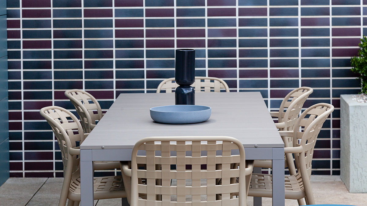 Outdoor dining table with woven beige chairs against tiled wall