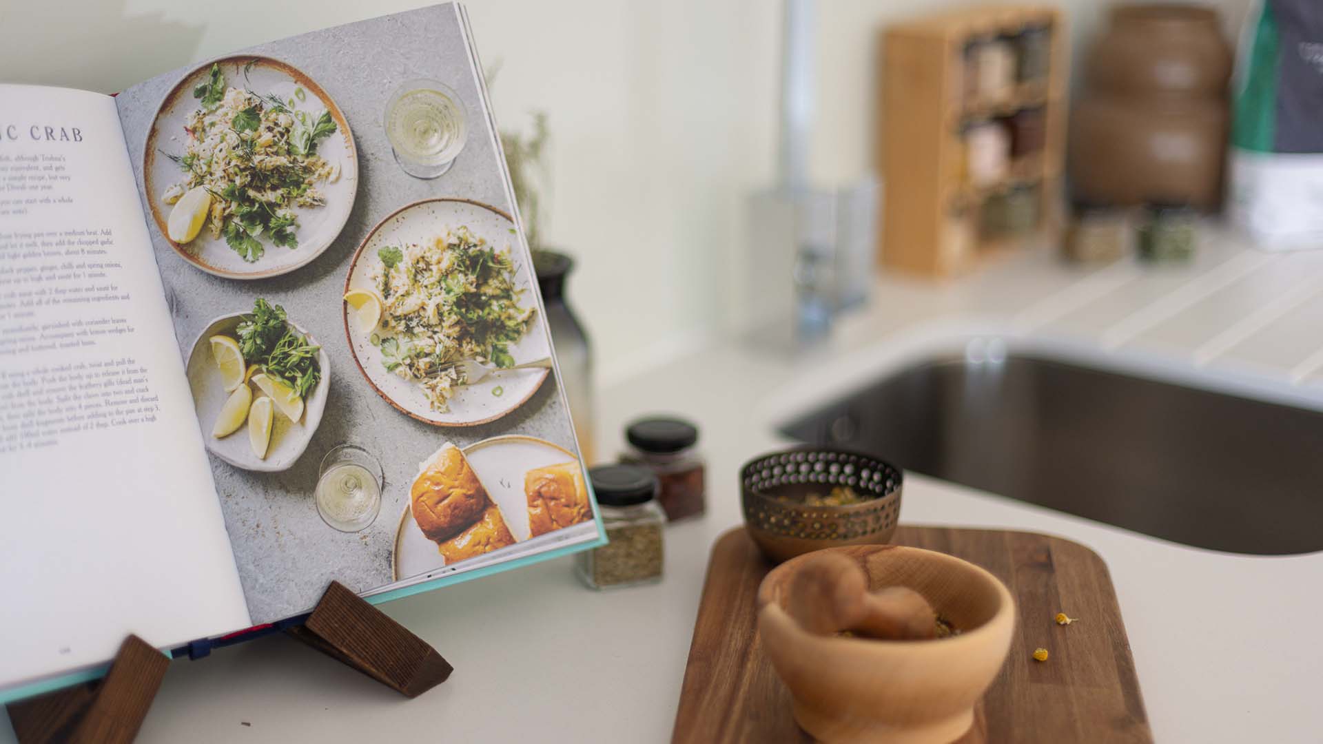 Open cookbook on kitchen counter with herbs and spices