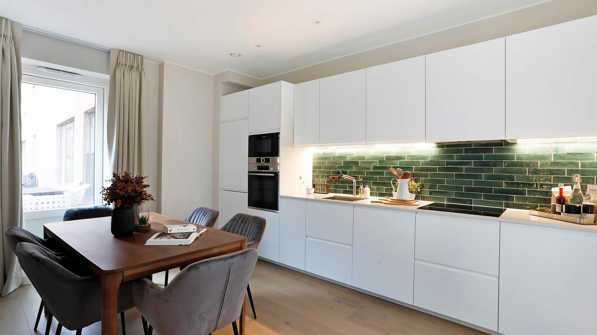 kitchen with white cabinetry, green subway tile backsplash, and wooden dining table