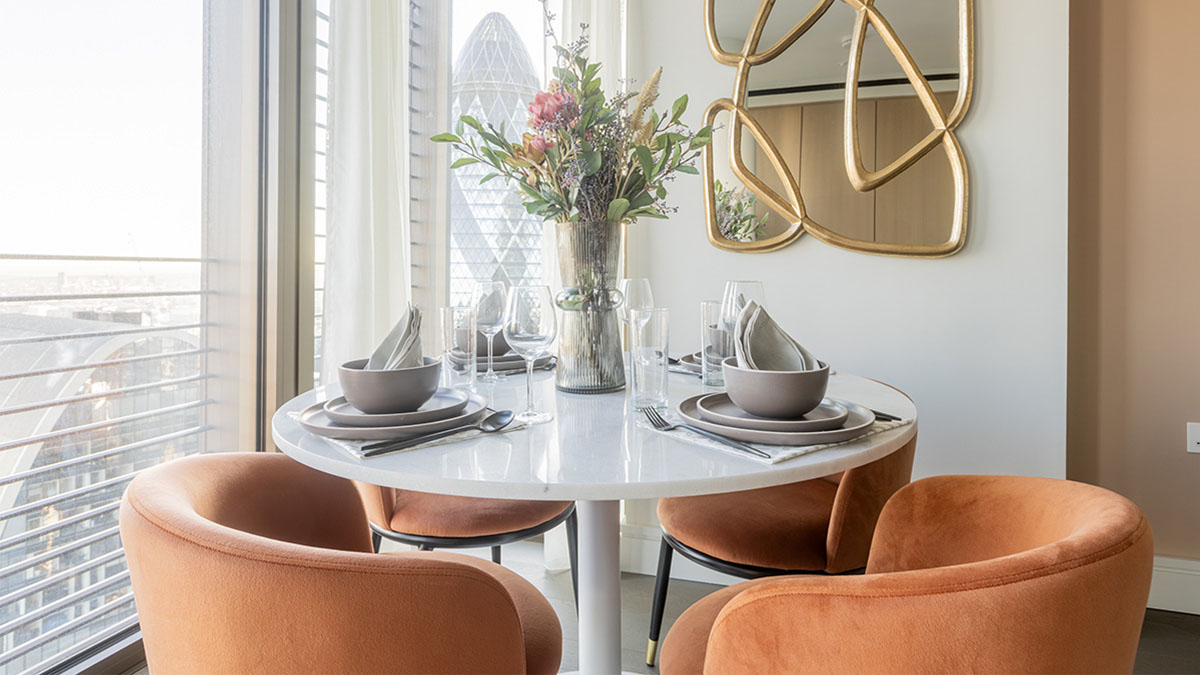 Modern round dining table with orange velvet chairs and Gherkin building view in London 