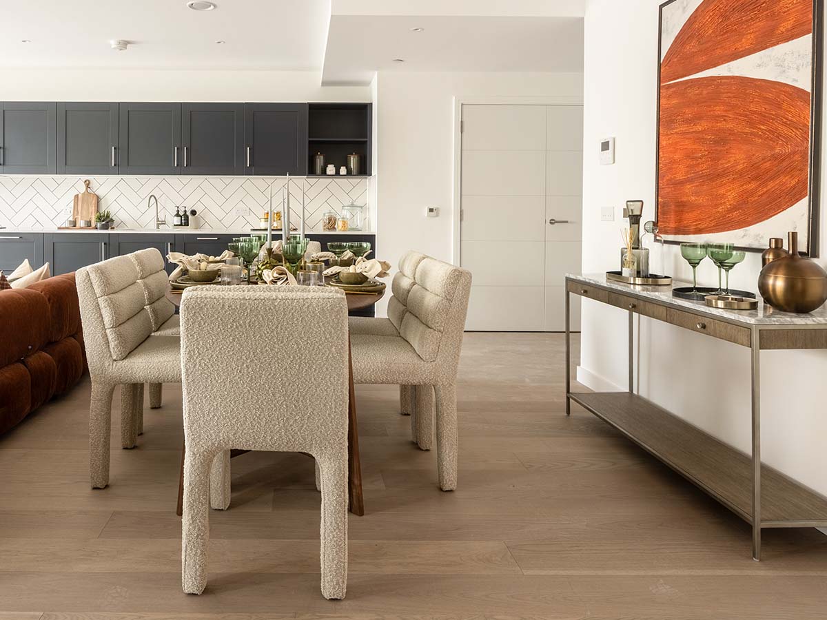 Modern open-plan kitchen and dining area in a Fulton and Fifth London flat, featuring dark blue cabinets, light dining chairs, and a styled console with abstract art