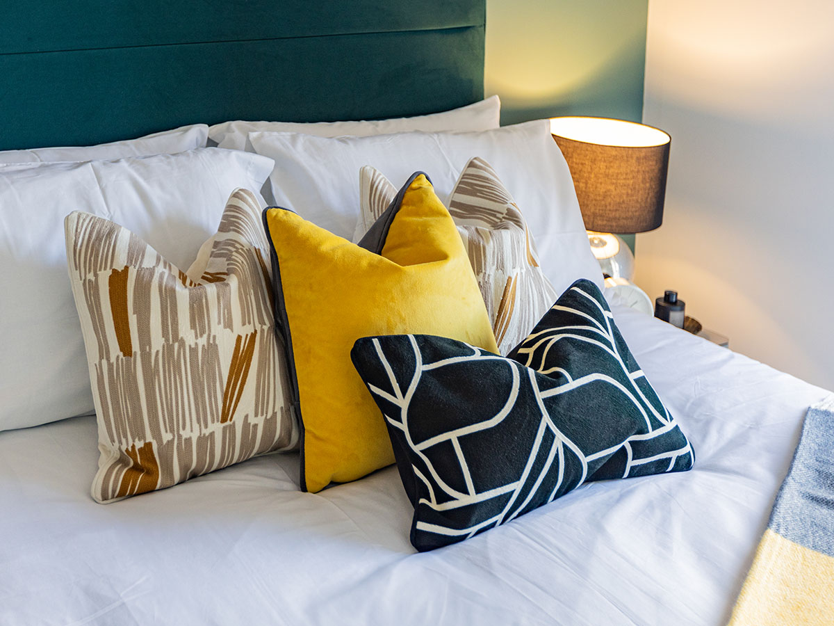 Close-up of soft white pillows with various patterned and solid yellow decorative cushions on a bed in a London flat bedroom