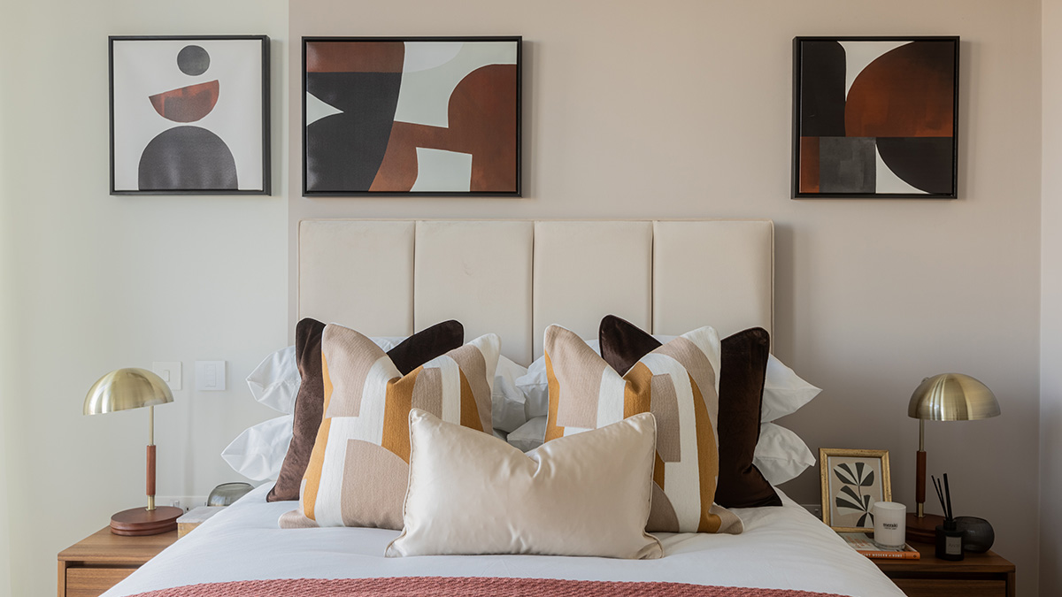Modern bedroom with neutral headboard, abstract wall art, and layered geometric cushions 