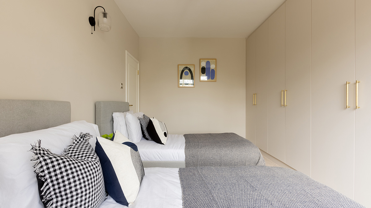 Staged bedroom with two twin beds, grey headboards, decorative pillows, and floor-to-ceiling wardrobes at 48 Montrose Court