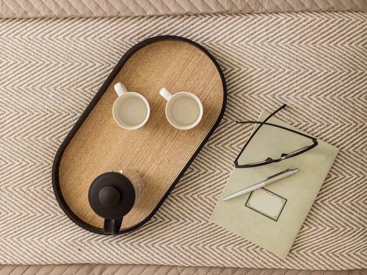 Overhead view of a stylish bedside setup with coffee cups and a notebook, highlighting Oval Village furnishing details