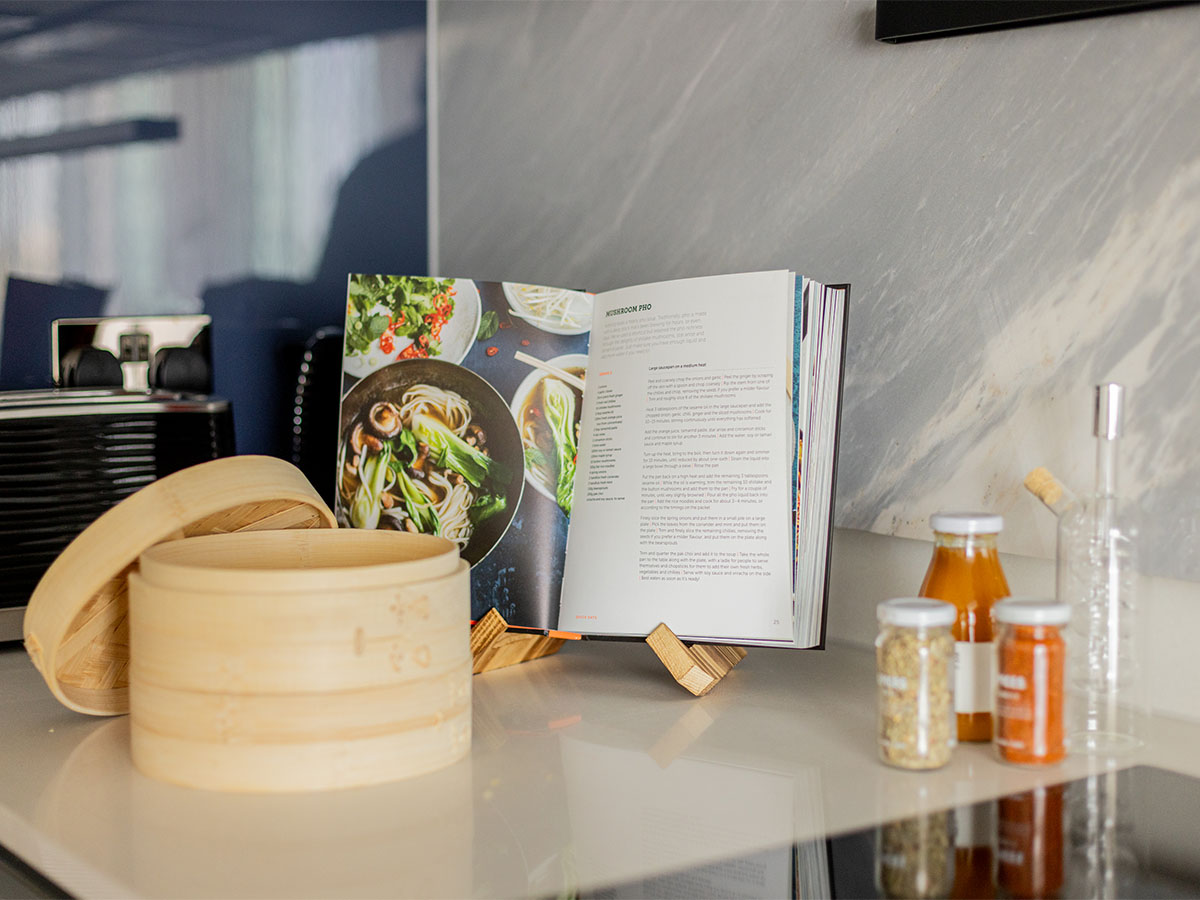 Open cookbook on a stand in a modern Oval Village kitchen, with various ingredients and a bamboo steamer