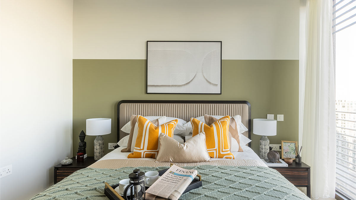 Bright bedroom with green accent wall, orange pillows, modern headboard, and breakfast tray