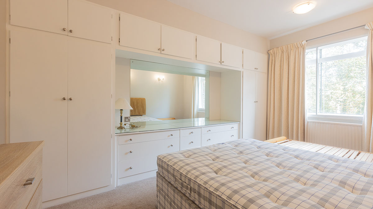 Outdated bedroom with mismatched cabinetry and patterned mattres