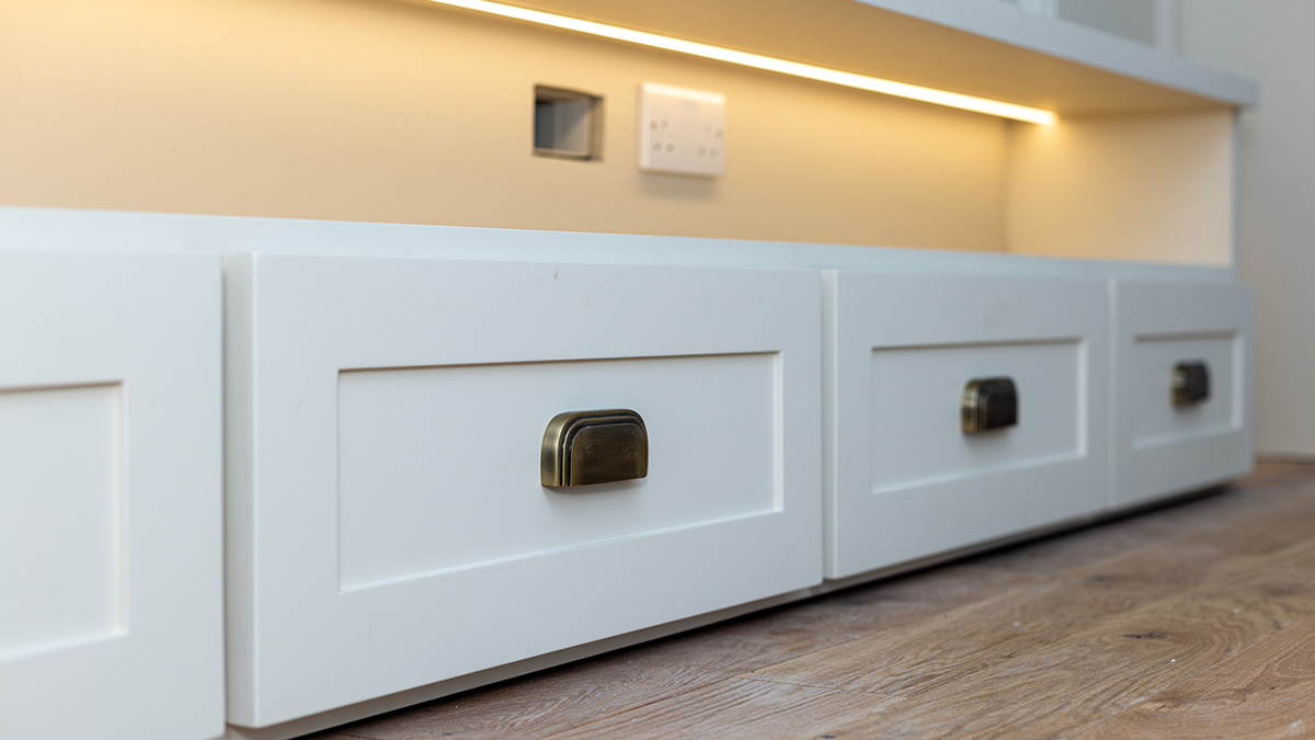 Built-in white cabinetry with antique brass handles and integrated under-shelf lighting, illustrating bespoke furnishing in a London flat