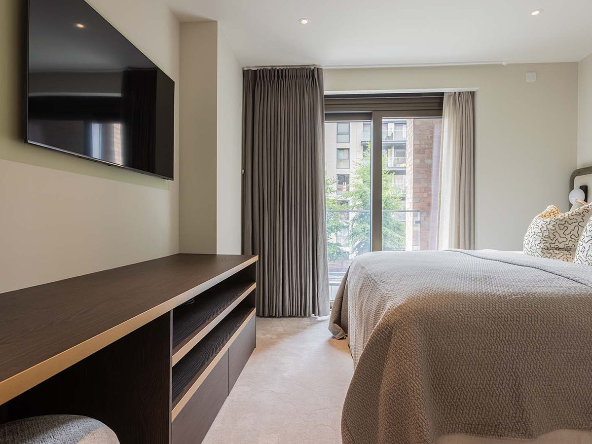 Furnished master bedroom in a Heron Wharf apartment with a dark wood media console and balcony access