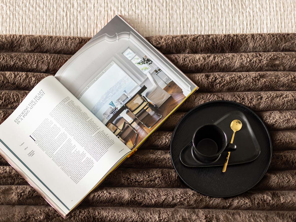 Close-up of a stylish magazine and black tray with a coffee cup on a textured brown bedspread in a London flat bedroom