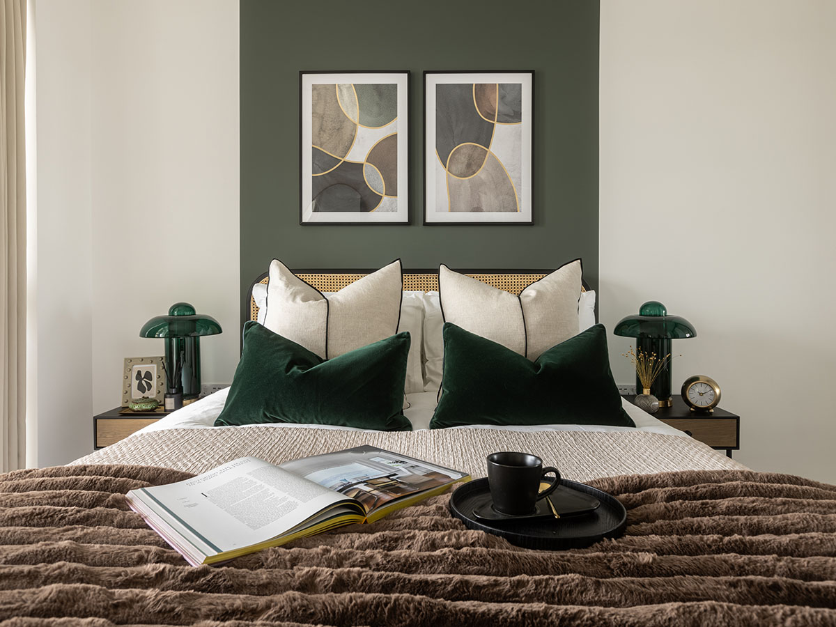 Master bedroom in a London flat with a rattan headboard, dark green accent wall, and elegant bedside lamps, furnished by InStyle Direct