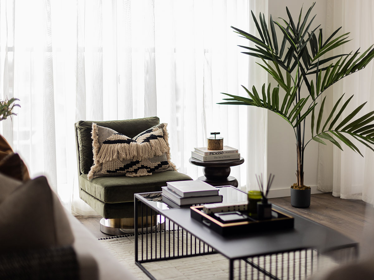 Cozy reading nook in a London flat with an olive green armchair, decorative cushion, and indoor plant, showcasing professional interior design