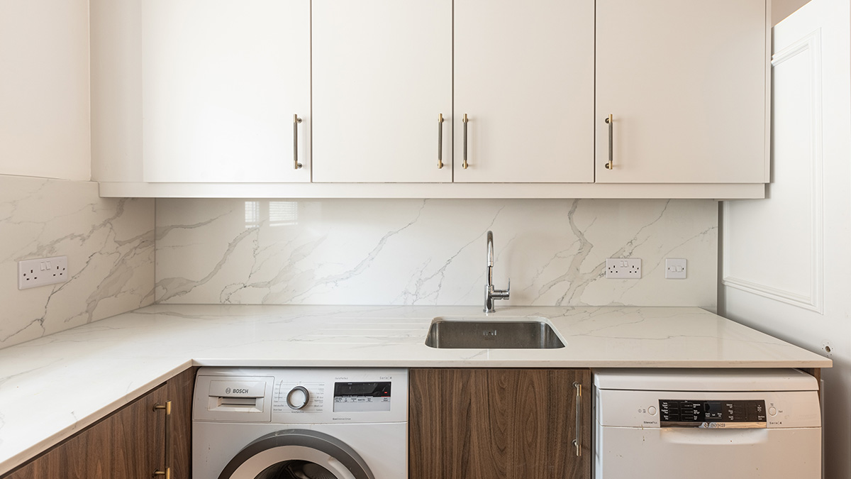 Modern utility room in a London flat with white marble-effect countertops, white cabinets, and integrated washing machine, showcasing a professional renovation