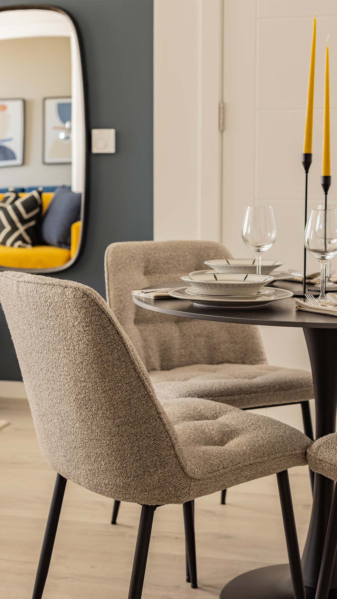 Professionally furnished dining area in a London flat, featuring a round black table, light grey upholstered chairs, and a table setting with yellow candles