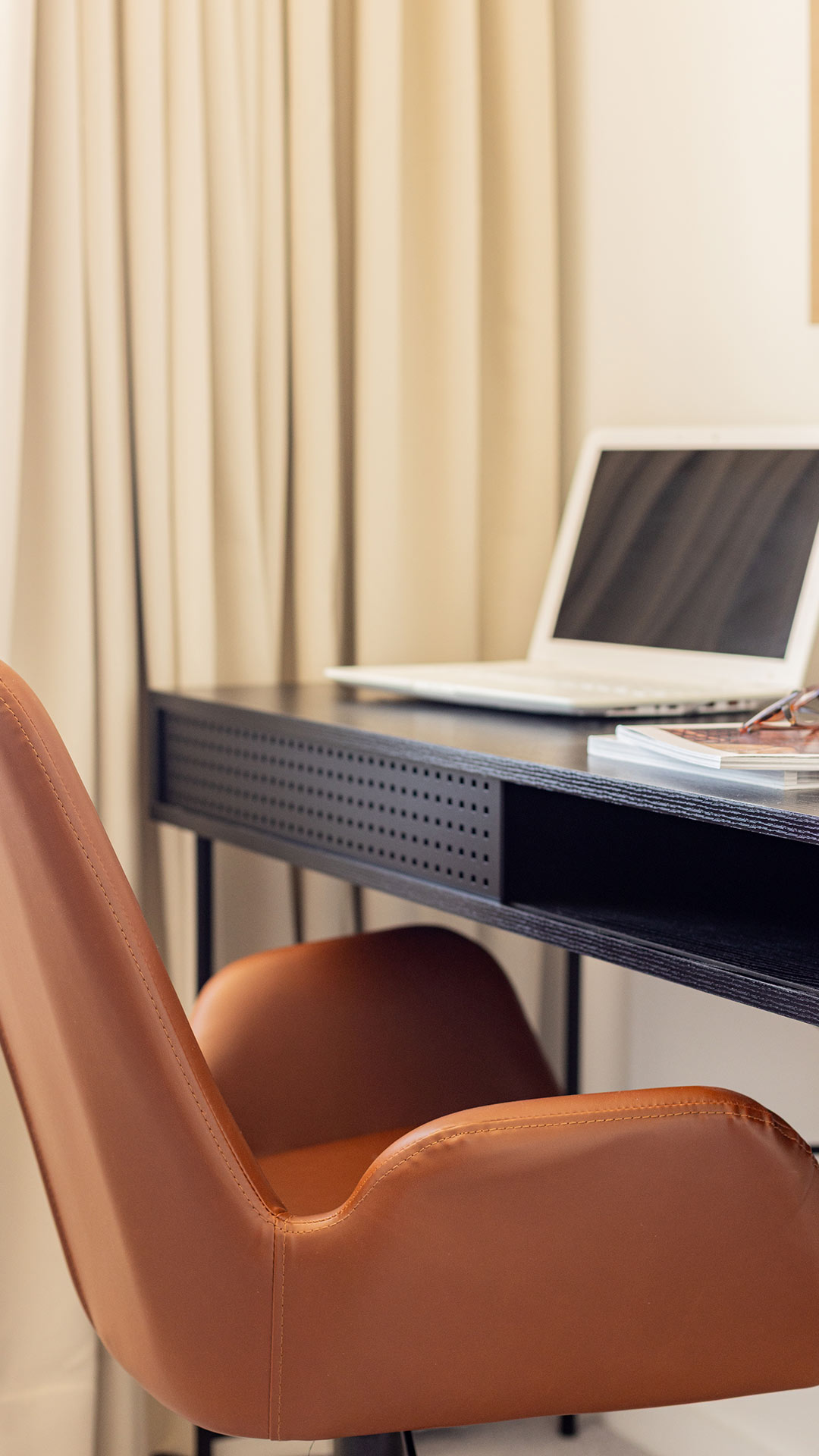 Stylish home office desk with a laptop and a brown leather chair, demonstrating a functional workspace in a Meridian One London flat