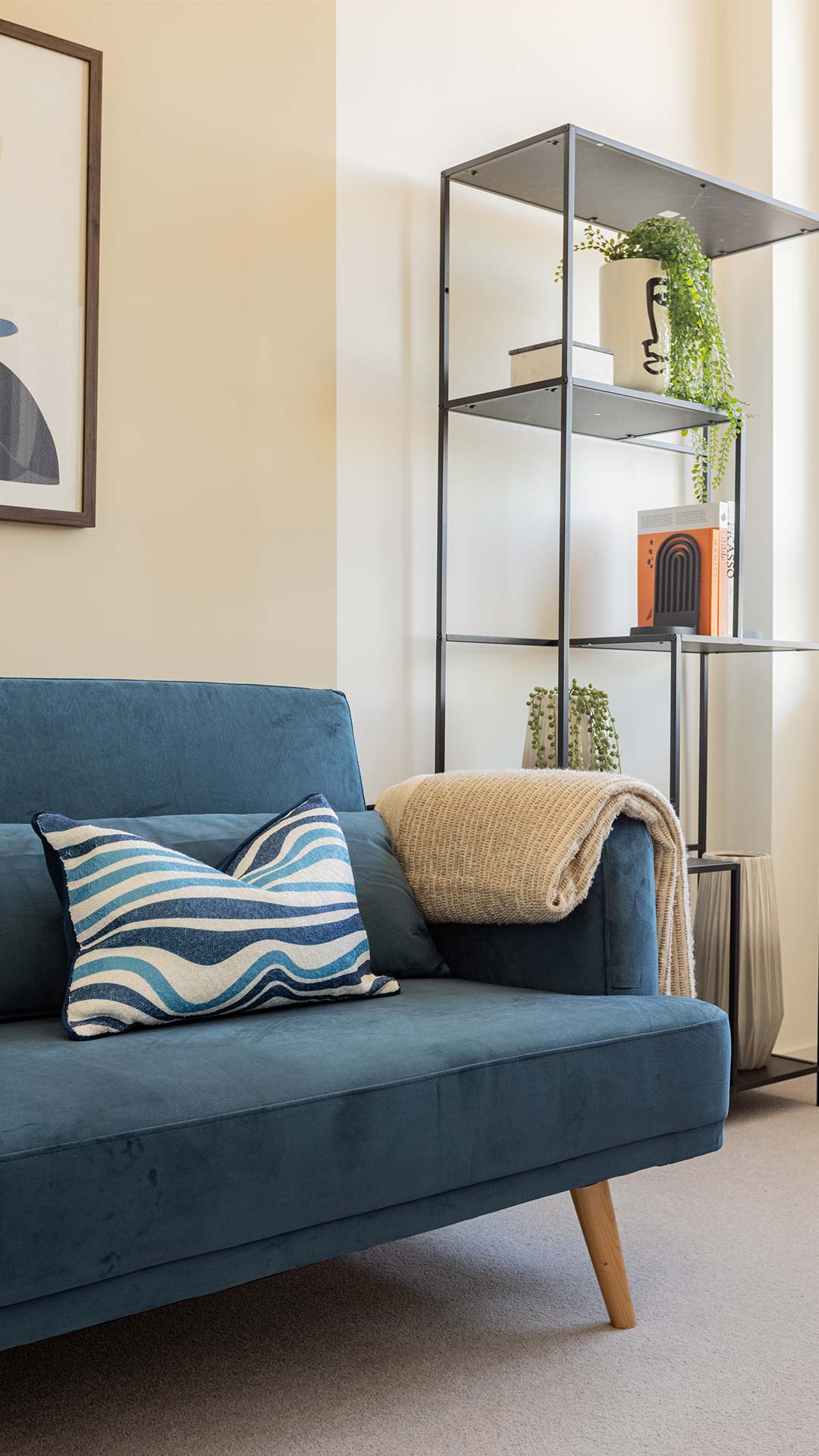 Blue sofa with a striped pillow and a throw, beside a stylish black bookshelf with decor, in a Meridian One living room