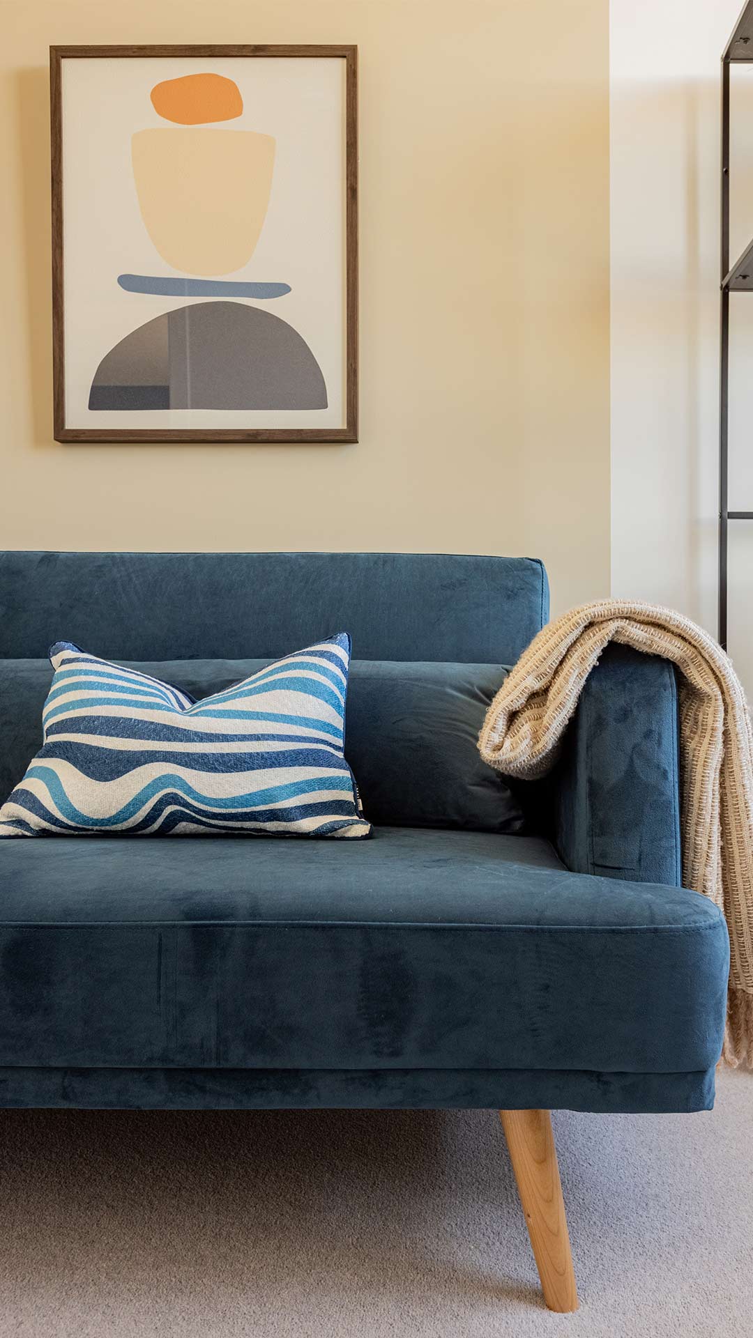 Close-up of a comfortable blue sofa with a striped pillow and a throw, under abstract wall art, in a Meridian One London flat