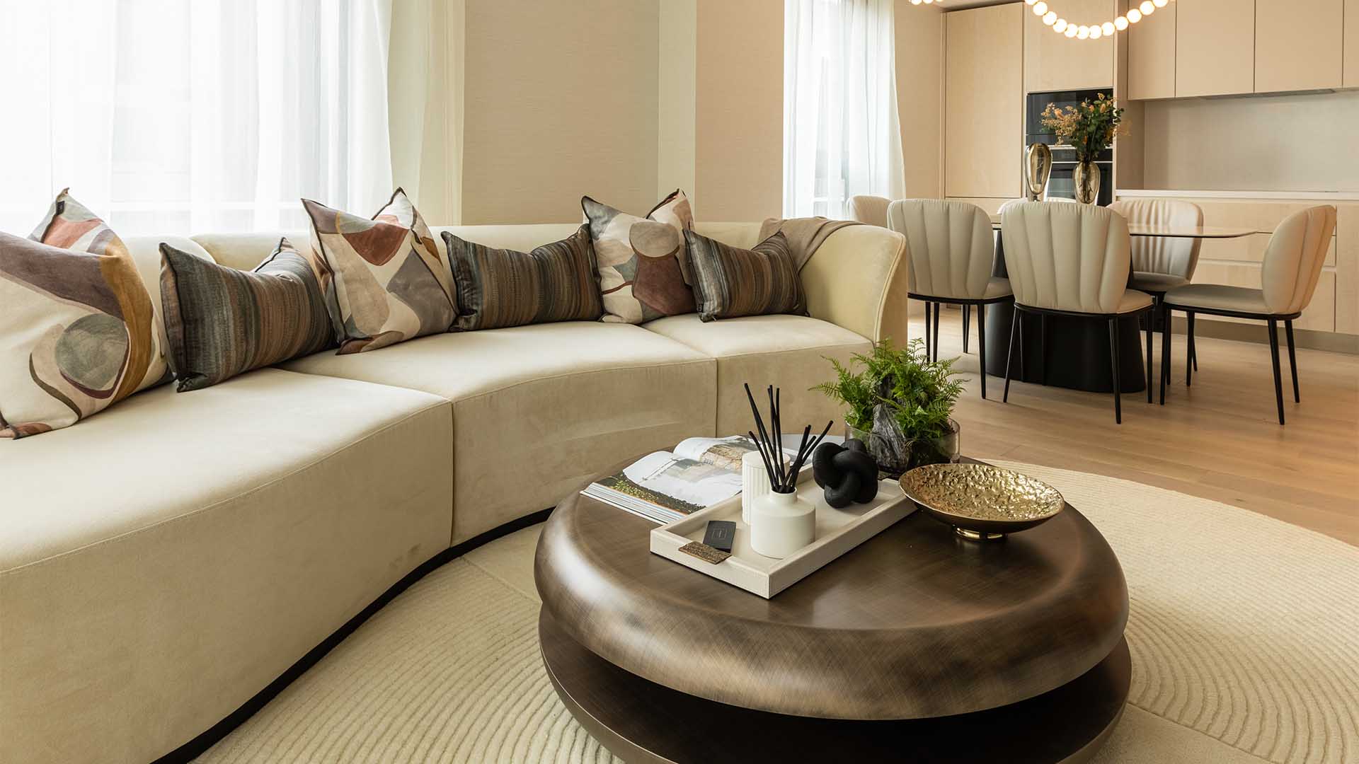 A professionally furnished living room with a curved sofa and round coffee table, demonstrating a transformation for a London flat
