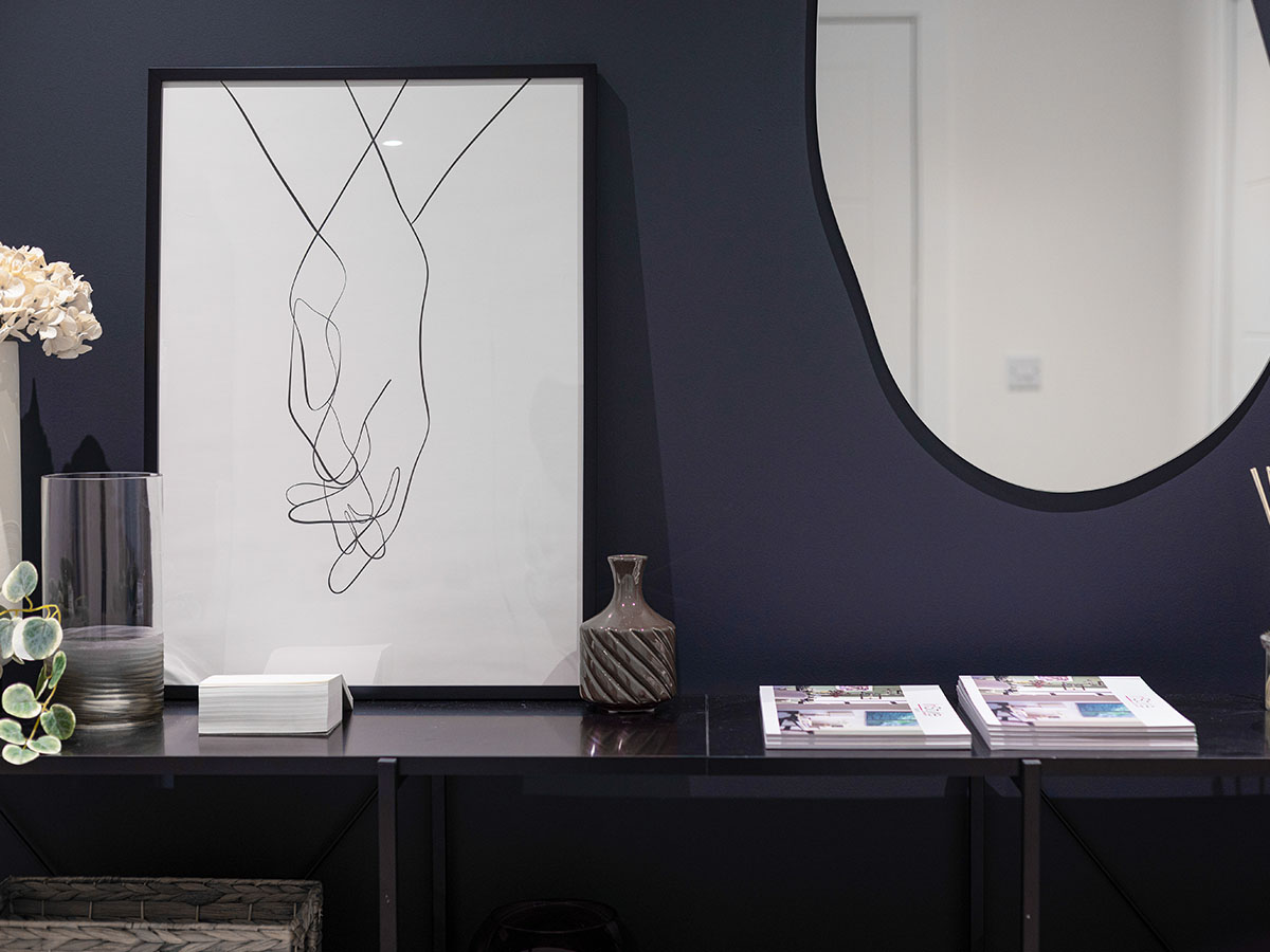 A styled black console table in the hallway at Cargo House, featuring a minimalist line-art print of holding hands against a dark blue wall