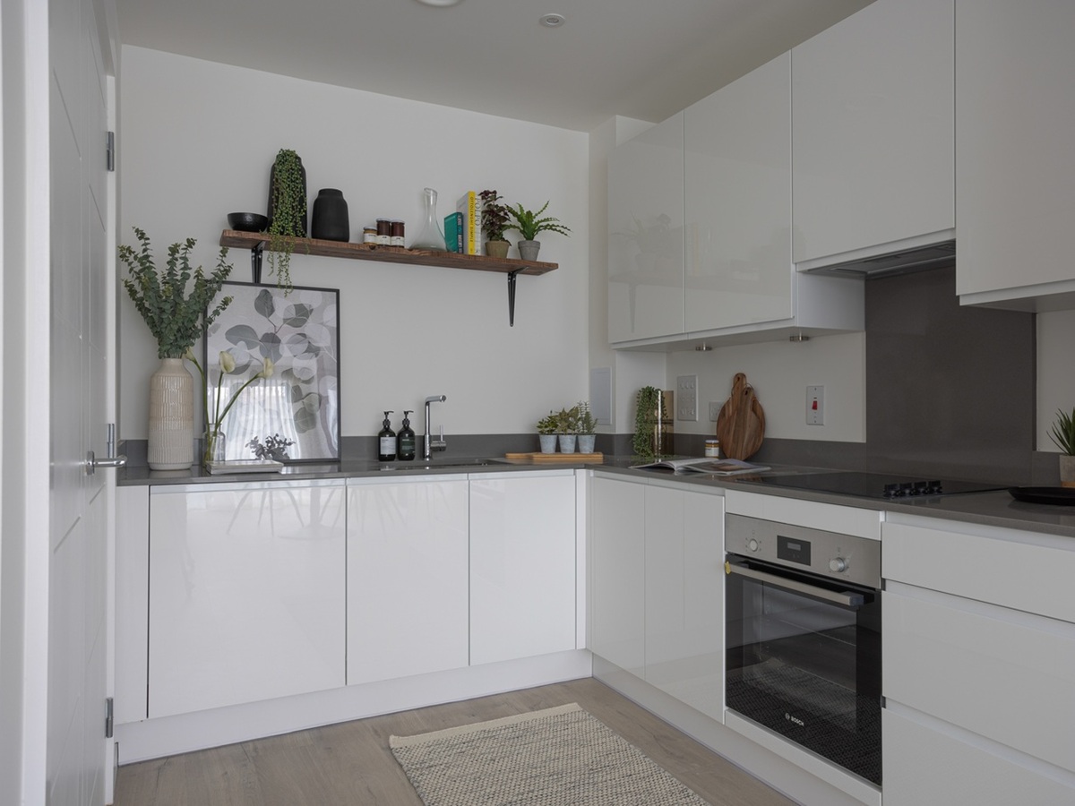 The L-shaped modern kitchen at Cargo House, featuring white high-gloss handleless cabinets, grey countertops, and stylish decor including plants and botanical art