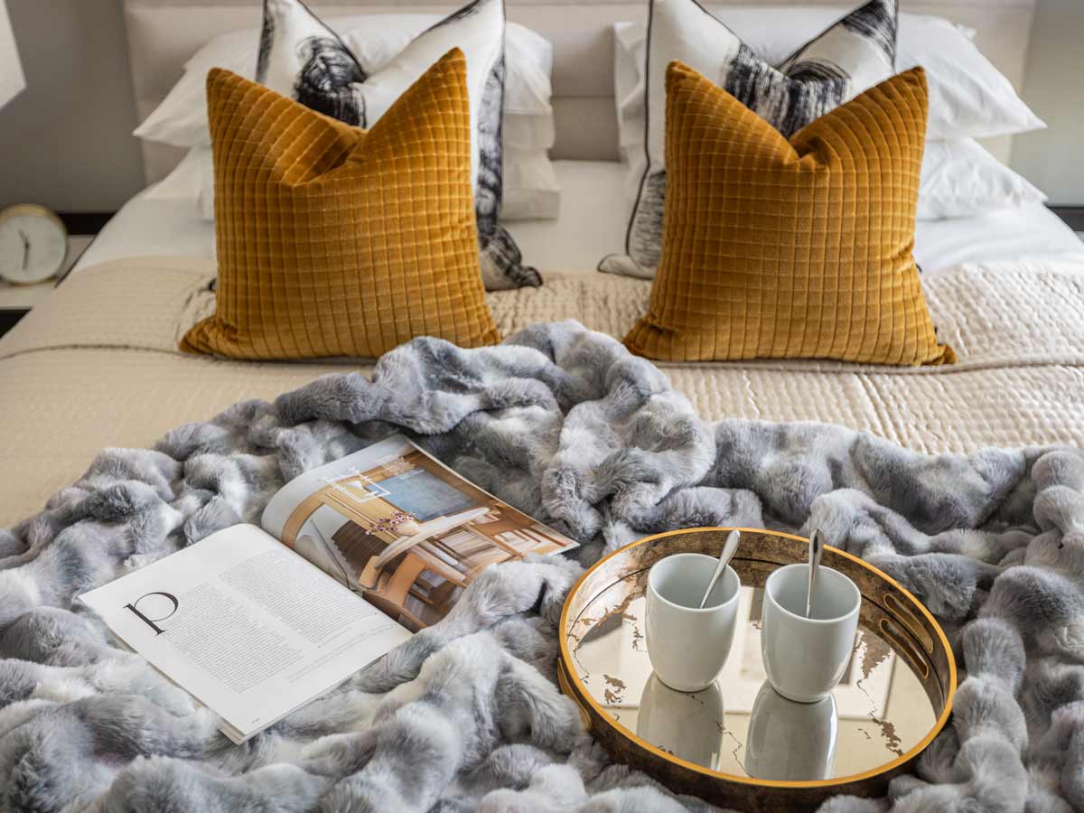 A stylishly made bed at Koa House with a grey faux-fur throw and a breakfast tray