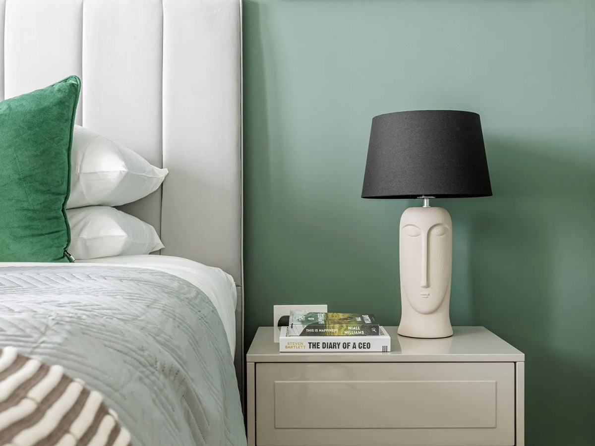 A detail shot of a show home bedroom designed for developers, featuring a statement sculptural lamp and a sage green wall for an aspirational feel