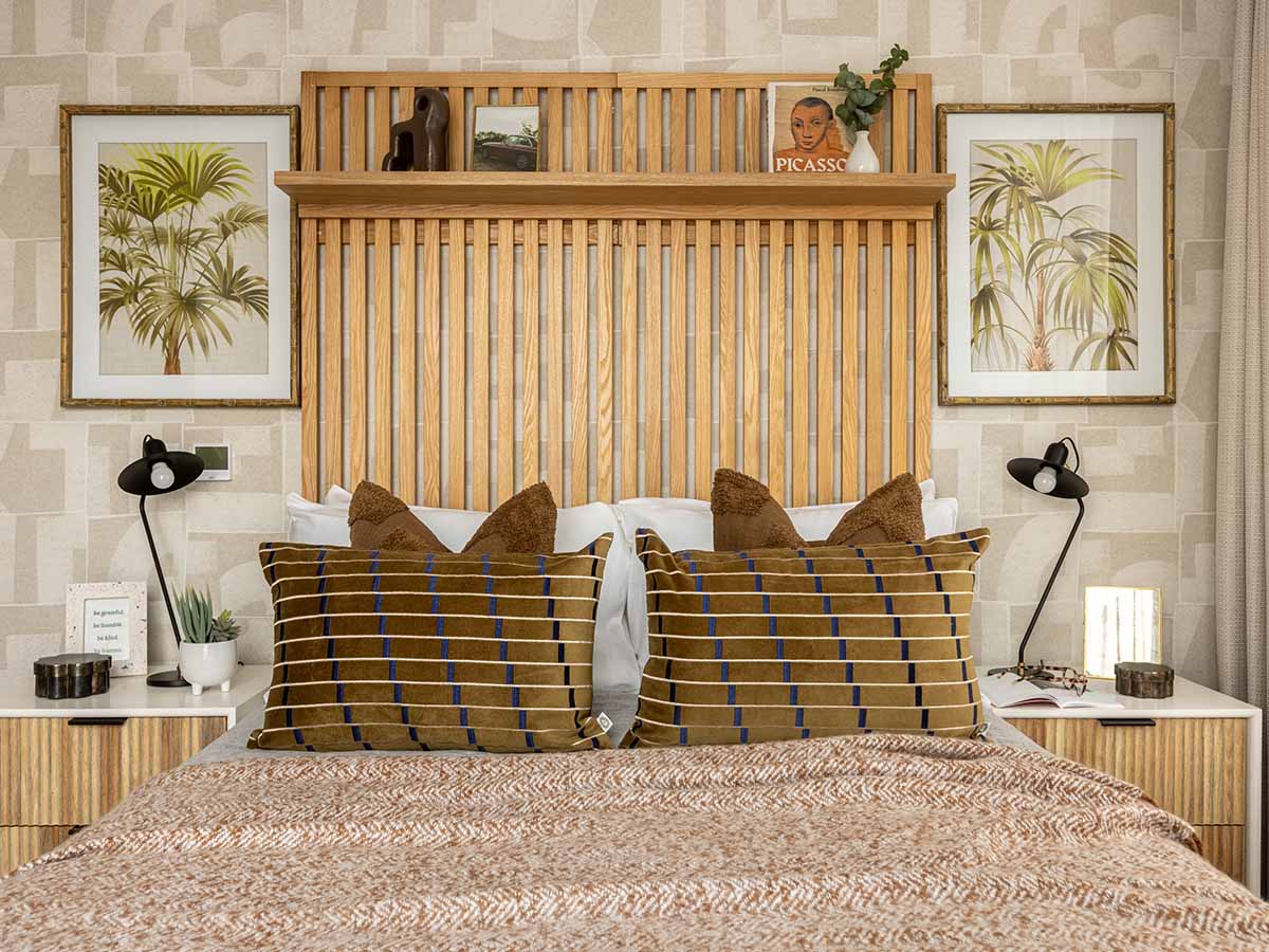 A stylish bedroom at Fulton & Fifth featuring a large slatted oak headboard with a display shelf, geometric wallpaper, and framed palm tree art