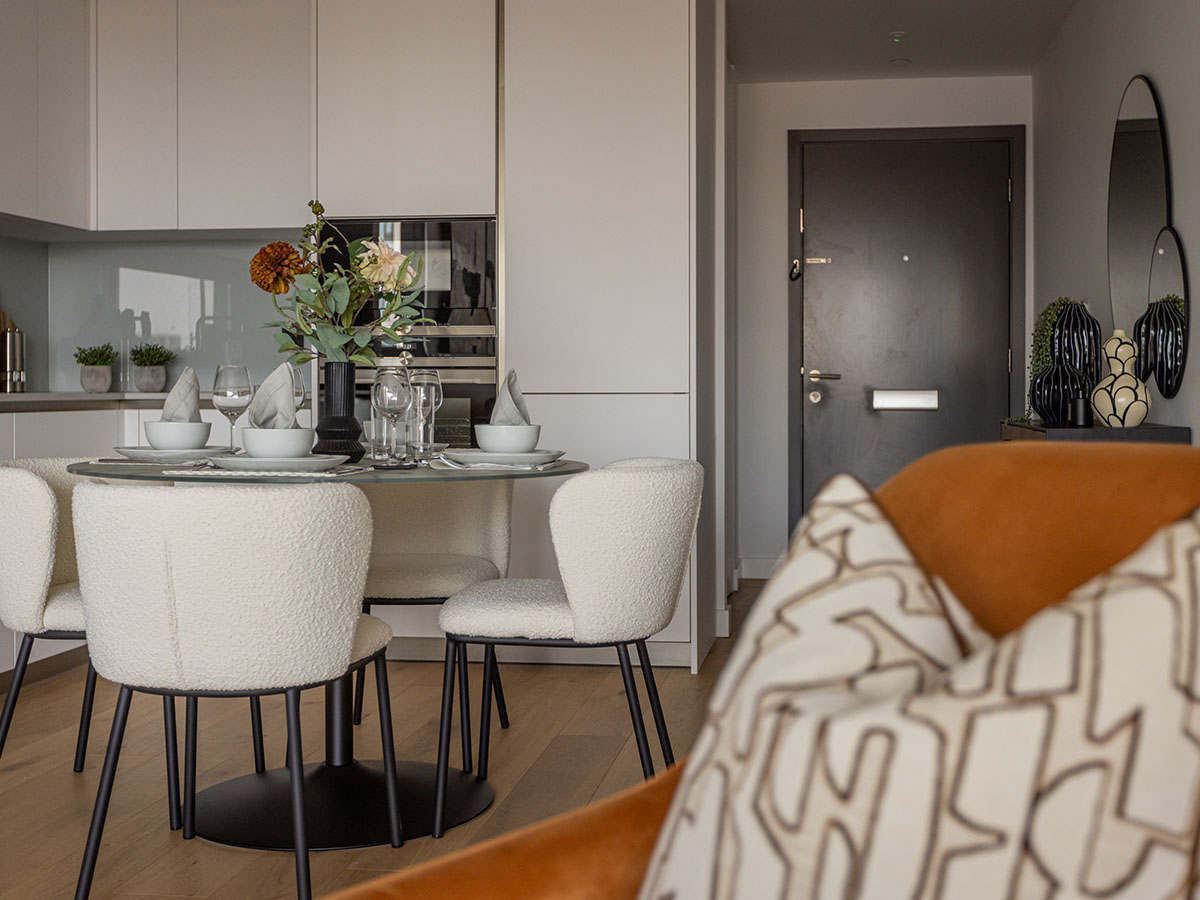A modern dining area at Koa House featuring a round glass table surrounded by white bouclé fabric chairs, with the sleek kitchen in the background