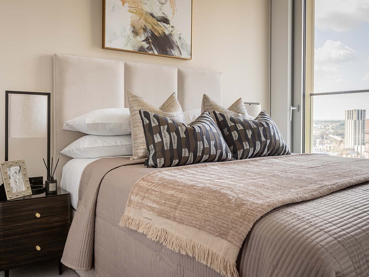 A luxurious bedroom at Koa House with a cream channel-tufted headboard, geometric print cushions, and a large window overlooking the citydining-area