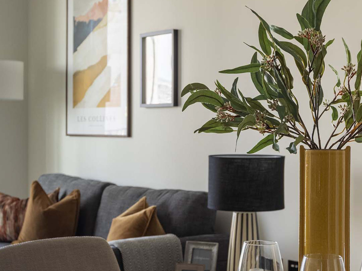 An artfully styled living room detail at White City Living, showing a yellow vase with eucalyptus in front of a grey sofa and modern abstract art.
