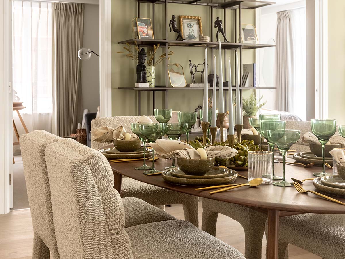 An elaborately set dining table at Fulton & Fifth, Wembley, featuring green glassware, gold cutlery, and textured boucle chairs for a luxurious feel