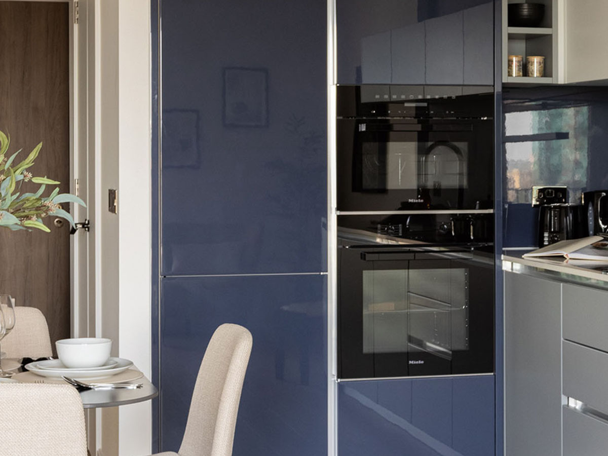 A sleek, modern kitchen at White City Living featuring high-gloss blue handleless cabinets and integrated Miele double ovens.