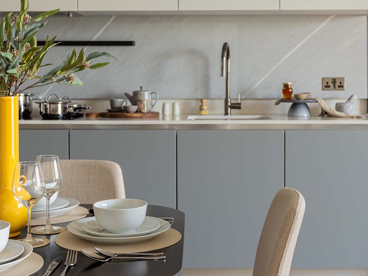 A modern kitchen at White City Living with matte grey handleless cabinets, a light grey marble-effect backsplash, and a styled dining table in the foreground.
