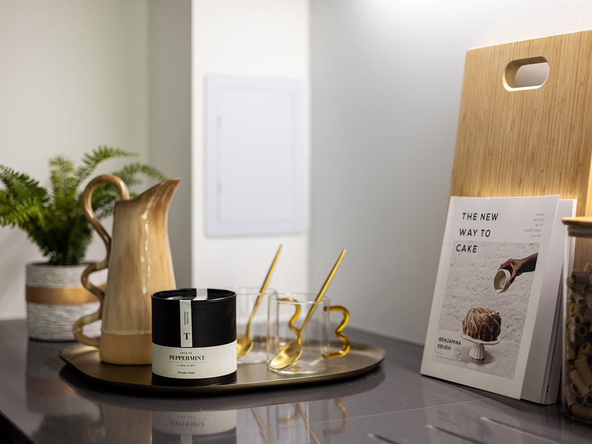 A close-up of a styled kitchen counter at The Auria, with a decorative brass tray holding a scented candle, mugs, and a cookbook.