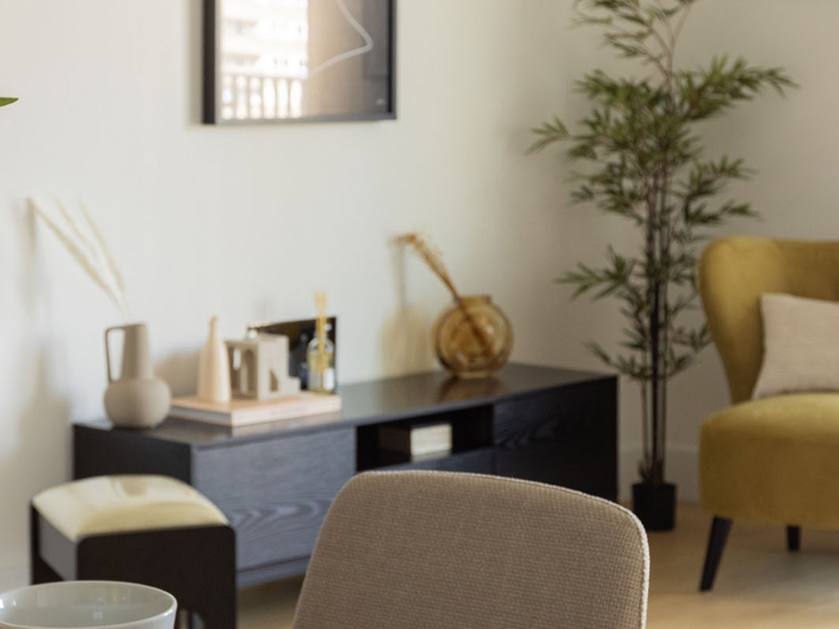 A styled living room corner at White City Living, featuring a yellow armchair, a tall plant, and a modern black media console