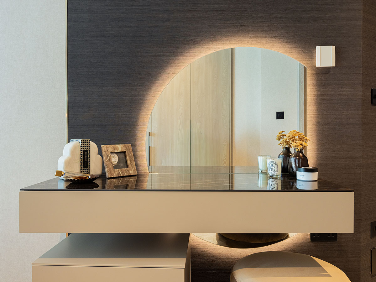 A bespoke dressing table area in the Aspen apartment, featuring a floating vanity and a large, arch-shaped mirror with integrated backlighting